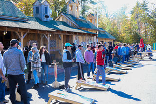 Players lined up tossing bags in a multi-lane cornhole setup outside the pavilion