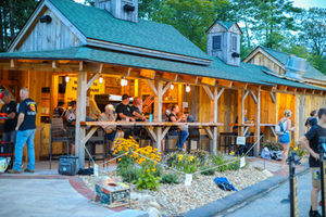 People enjoying drinks and conversation on covered porch with wooden beams at The Barnyard