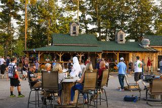 Guests seated at outdoor tables near pavilion with drinks and food on a fall day