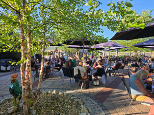 People seated on patio under trees and umbrellas at The Barnyard during a lively bingo night