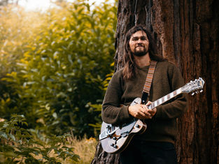Samuel Ashton playing guitar by a tree