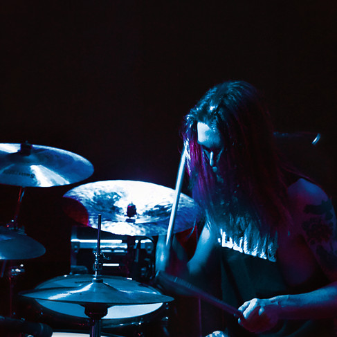 A band member on the drums with a primary blue light on the scene.