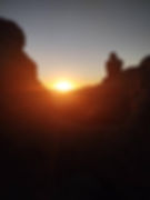 Silhouette of a person sitting on rocks with a glowing sunset in the background, creating a serene and contemplative atmosphere.