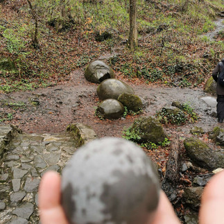 Hand, die eine kleine Steinkugel hält, die aus Fragmenten, einer großen Steinkugel geformt wurde, die man im Kugelwald von Zavidovici in Bosnien zerstört hatte, um ihrem Geheimnis auf die Schliche zu kommen
