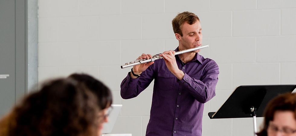 Flutist in a purple shirt performing in a classroom setting.