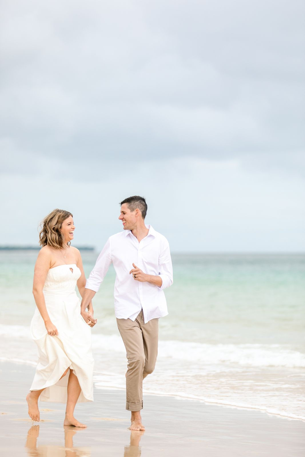 Just married couple walking on the beach hand in hand laughing and smiling