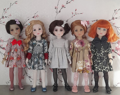 Cinq poupées Fashion Friends alignées, portant des Petites Robes Maison Méricourt aux motifs floraux et aux couleurs variées, photographiées dans une scène douce et élégante.