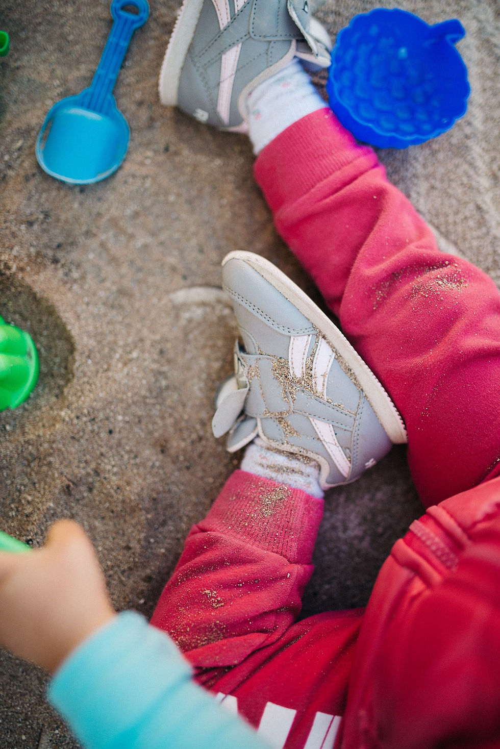 Child sitting in sand beside a toy shovel and colorful sand molds.