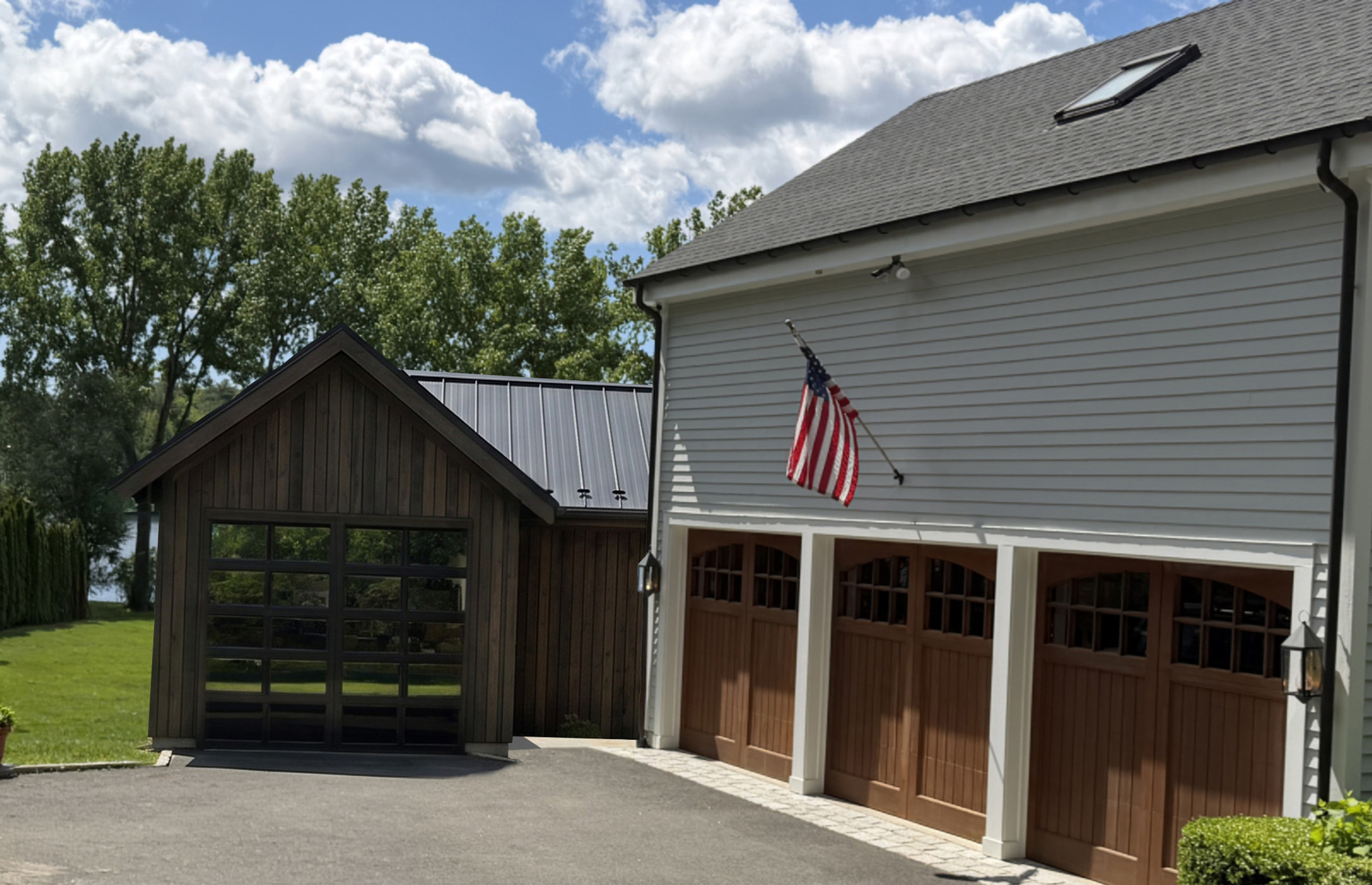 Small dark wood outbuilding beside a light gray garage with wooden doors