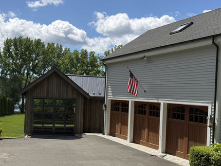 Small dark wood outbuilding beside a light gray garage with wooden doors