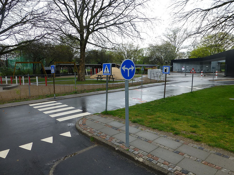 Miniature roads, pedestrian crossings, and traffic signs surrounded by grass and trees at a children’s traffic playground in Copenhagen.