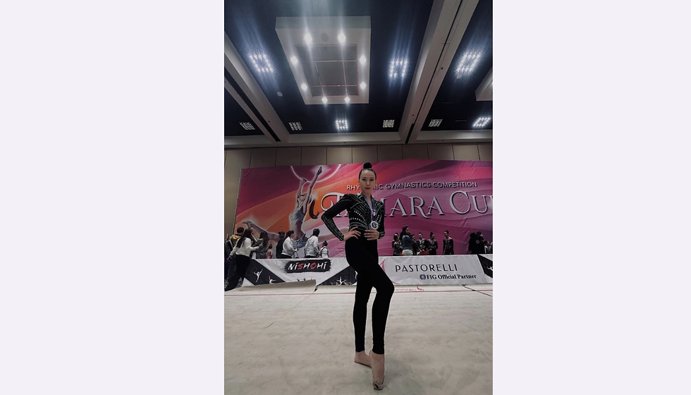 A gymnast wearing a black embellished outfit and a medal poses on the competition carpet.