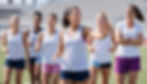 Female athlete leading her teammates through a warm-up while a woman coach watches supportively during practice.