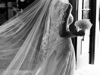 A black and white portrait of a destination bride in a lace dress walking towards the door of the chapel following the groom