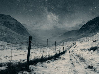 A snowy mountain valley with an old fence and the sky blanketed with stars.