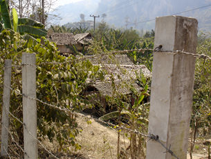 Thatched huts in a refugee camp seen through a barbed wire fence.
