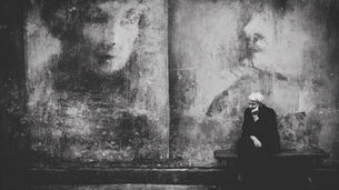 An old woman sits below a young woman's face.