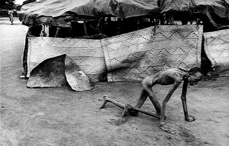 An emaciated man crawls along the ground.