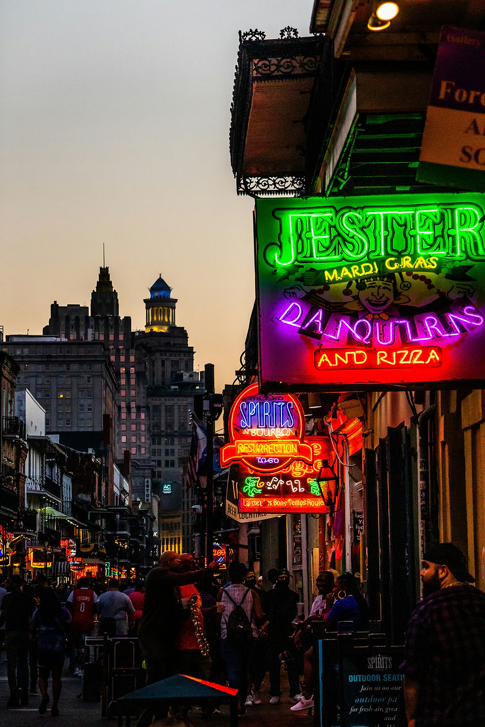 Crowded street in New Orleans at dusk, with people walking and colorful neon signs.