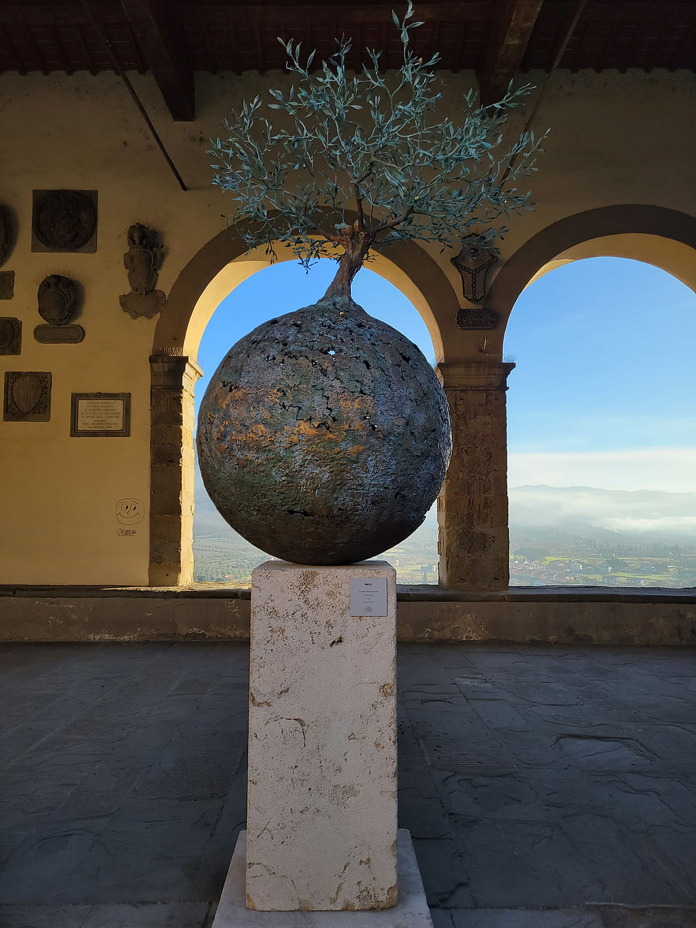 Bronze sculpture of a tree on a globe with a backdrop of arched windows into the valley