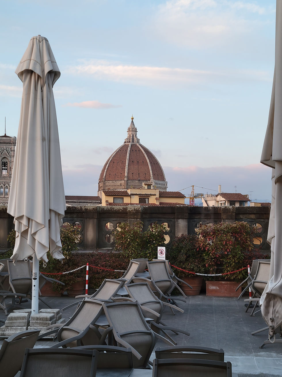 Rooftop view with stacked chairs and closed umbrellas. Florence cathedral dome visible in the background. Clear sky.