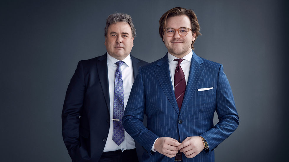 Per Skrealid står till vänster om sin son Gustaf Skrealid. Båda är klädda i kostym. Pers är svart och Gustavs är blå med tunna vita ränder. 