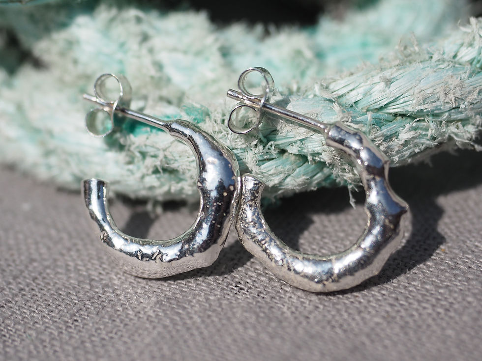Thumbnail: Half hoop earrings, silver and organically formed, shining in sunlight displayed on pale turquoise fishing rope.