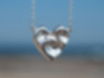 Triple ocean wave pendant in the shape of a heart infront of blurred beach backdrop