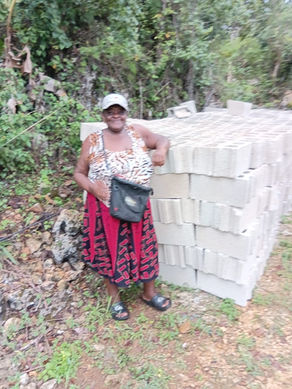 Alaiysha’s grandmother smiling beside a delivery of concrete blocks for rebuilding her home in Jamaica after Hurricane Melissa.