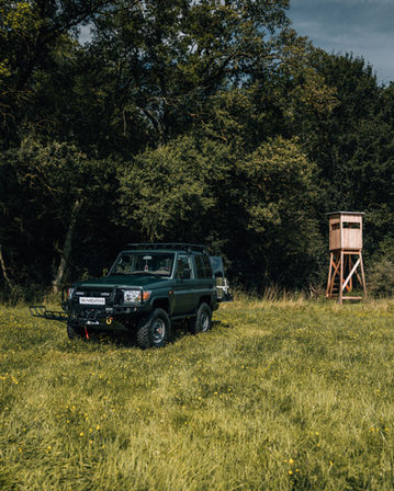Dunkelgrüner Geländewagen vor Hochsitz im Wald