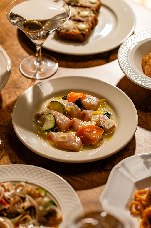 Crudo in broth with vegetables, next to a martini