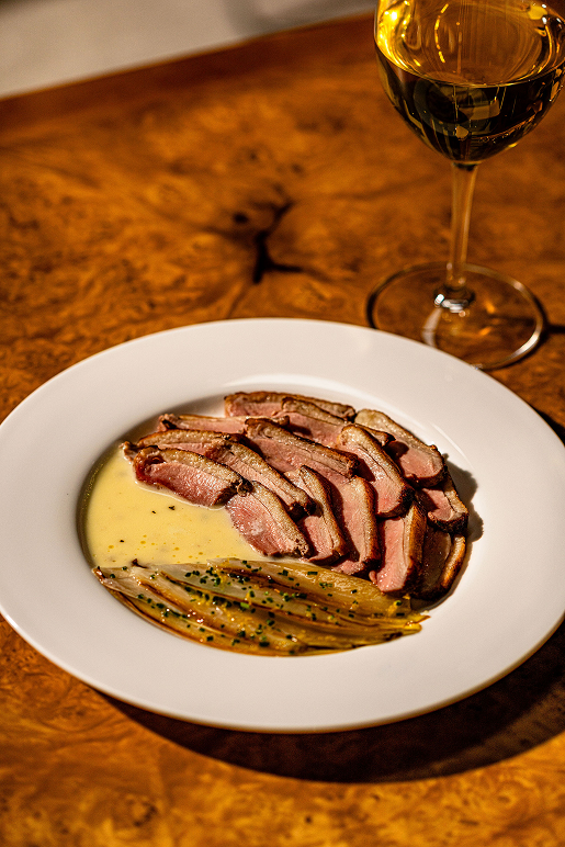 Sliced duck with sauce and a glass of white wine