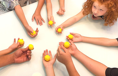תמונת תקריב של שש זוגות ידיים של ילדים שמחזיקים כדור צהוב מקליי
