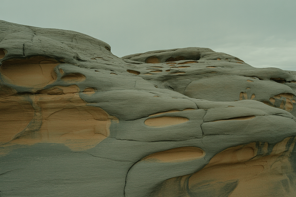 Superficie rocciosa naturale levigata da processi di erosione lenti e continui nel tempo, con strati di pietra arrotondati e cavità scavate visibili, sotto una luce neutra e uniforme, senza presenza umana, paesaggio ordinario che mette in evidenza la persistenza silenziosa delle leggi naturali ancora in azione.