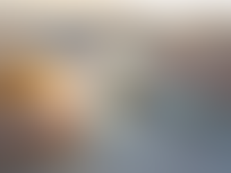 Paesaggio desertico immerso in una luce morbida, dove rocce stratificate e translucide sembrano formate dal tempo stesso, e una piccola pozza riflette un arcobaleno sottile, come traccia visibile della trasformazione irreversibile della luce nel suo viaggio.