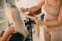 Faded background of hair stylist matching hair extension color to client hair