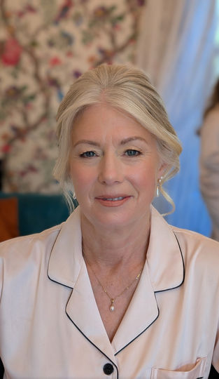 Elegant woman with silver hair smiles, BRIDAL, wearing light pink pajamas, indoors.