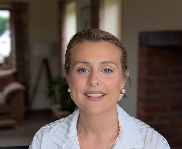 Smiling blond woman wearing a white shirt; indoor setting with neutral background.