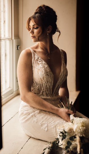 bride with dark hair up sat in a window smiling softly