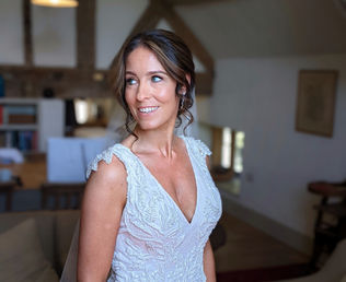 Smiling bride in white dress, looking away, wooden beam background, natural light.