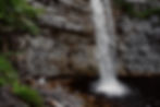 A couple in wedding clothes embraces next to a waterfall in the Catskills at Minnewaska State Park during their spring elopement.