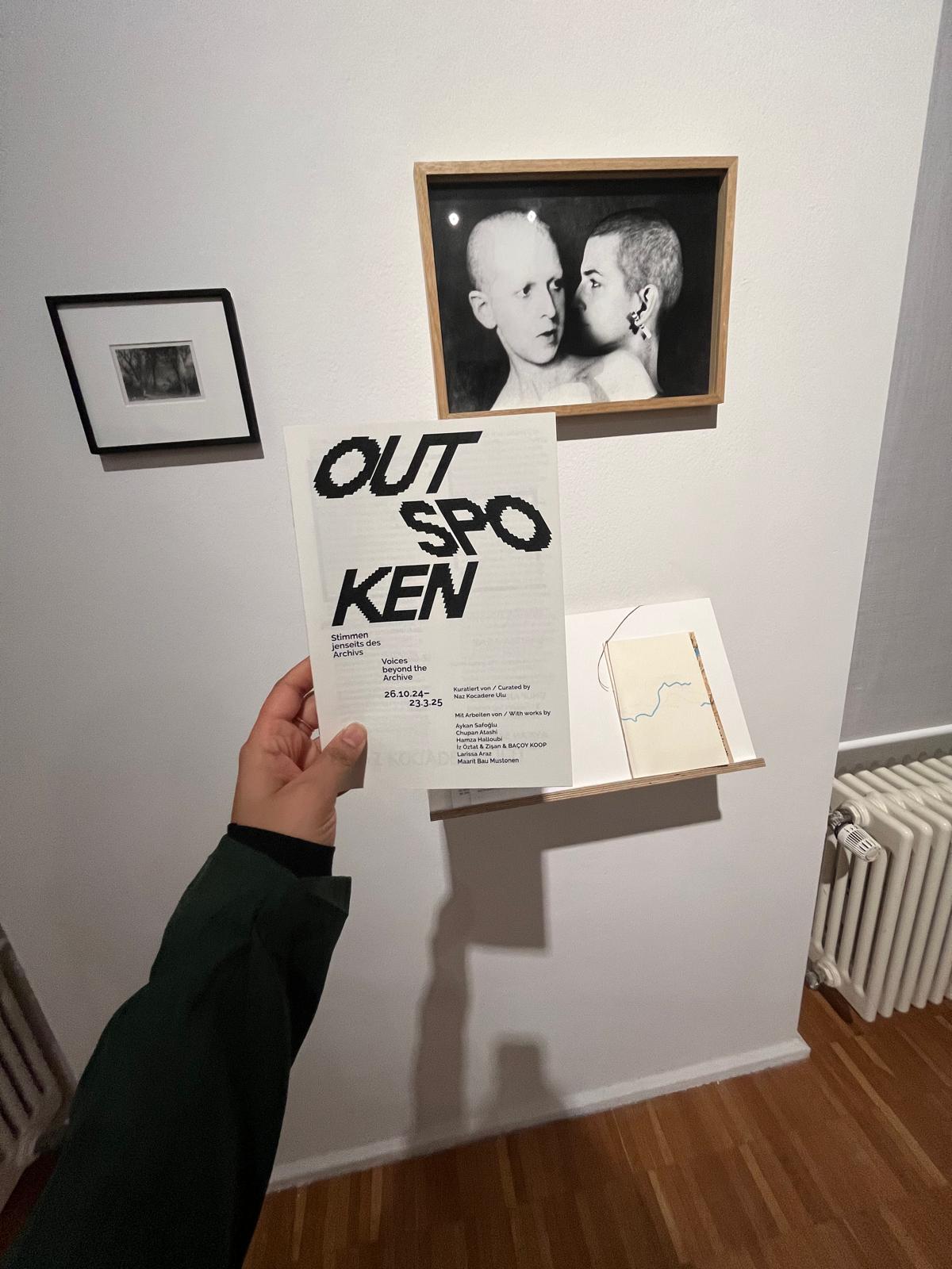 Hand holding a magazine with the text OUTSPOKEN near gallery artwork. Design Agency