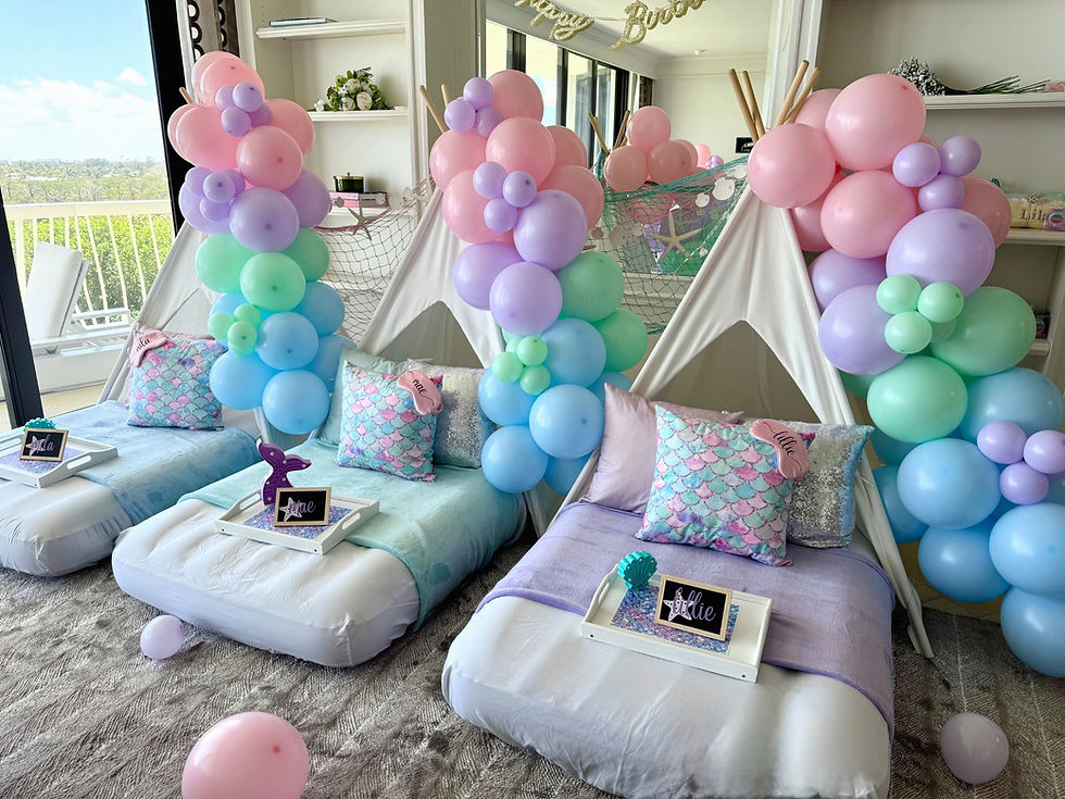 Mermaid themed teepee sleepover party setup with pastel balloon garlands, personalized trays, and cozy bedding