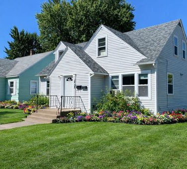 White house with green lawn and flowers, representing an as is home offer in Wausau.