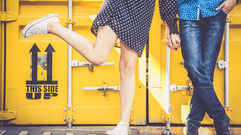 Couple holding hands standing in front of a large yellow shipping container.