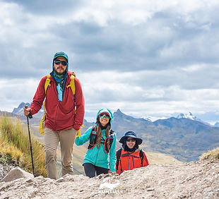 David, dressed in trekking gear, guiding 2 people up a rocky outcrop, with mountains and clouds in the background