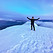 A climber standing on the summit of Cayambe holding his hands above his head in a triumphant manner, with a nice blue alpenglow sunrise behind him
