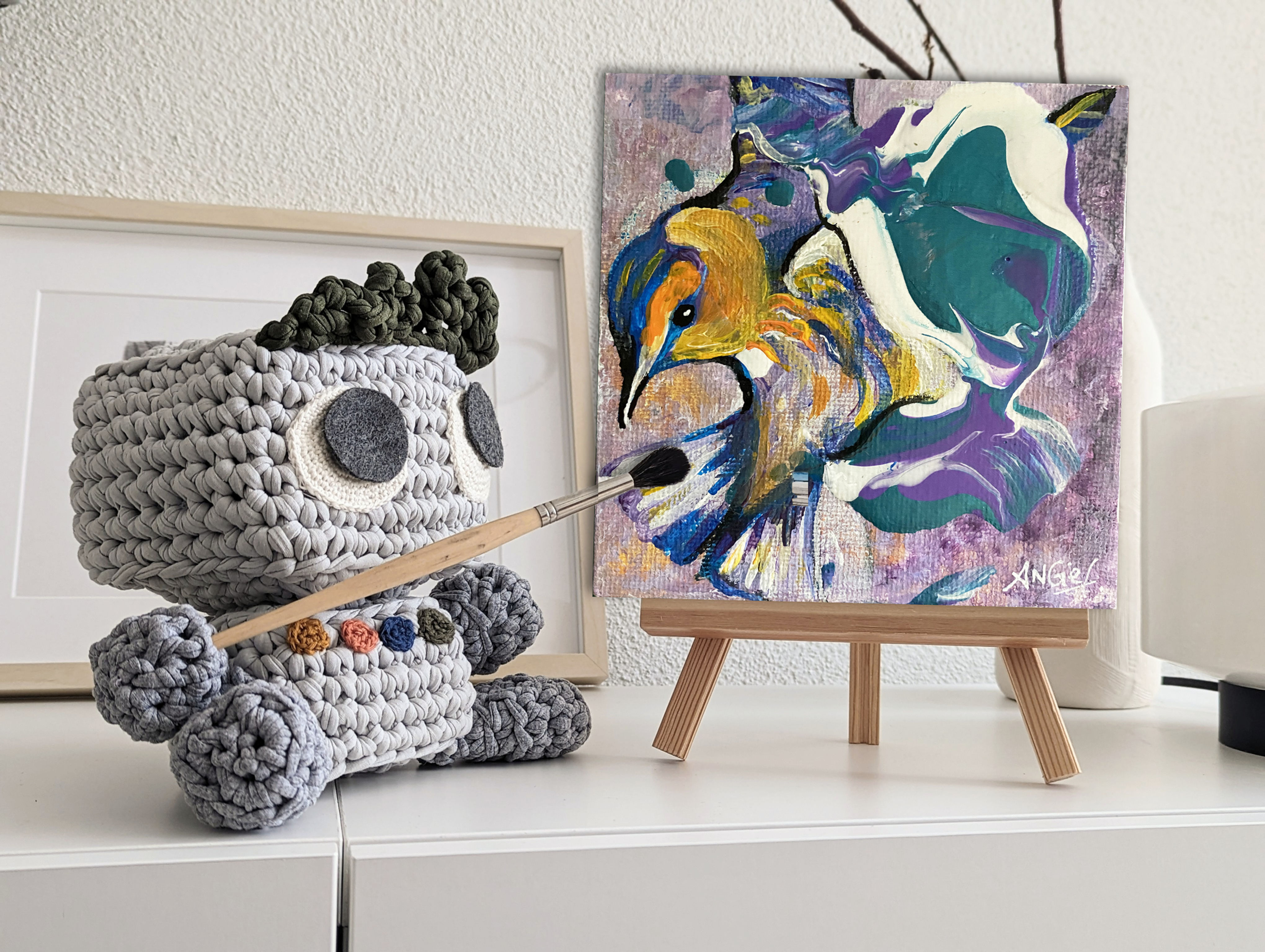 Mise en situation d'un oiseau bleu et orange sur mini chevalet. Réalisé à la peinture acrylique par l'artiste Angie F.