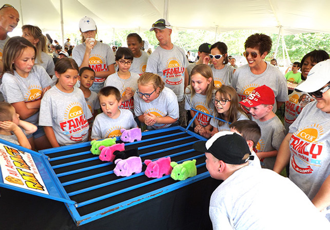 Kids and adults gathered around a stuffed animal pig race carnival game at a Picnic Master event.