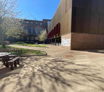 The outside of a college building with a bench and green areas on the left